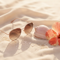 Lunettes de soleil, coquillage, hibiscus et sable sur soie — les cils face au soleil et à la mer en été